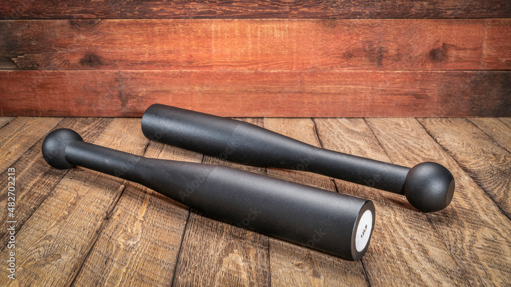 Obraz premium pair of heavy steel Indian clubs against rustic, weathered wood background - functional fitness concept, heavy clubs are particularly valuable for grip strength, and shoulder work,