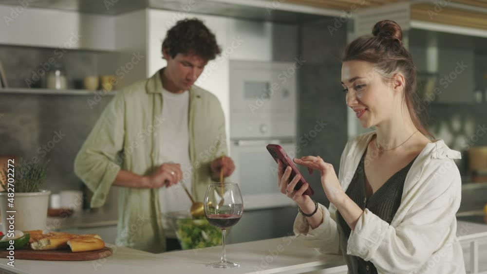 Man cooking salad while woman using smartphone Man cooking salad while woman using smartphone