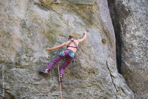 Determined girl climber clambering up steep wall of rocky mountain. Sportswoman overcoming difficult route. Engaging in extreme sports and rock climbing hobby concept
