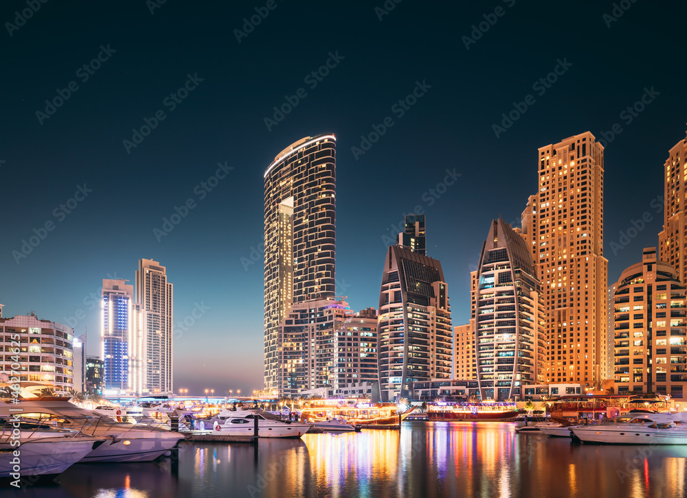 Dubai Marina Port, UAE, United Arab Emirates. Jetty With Many Moored Yachts, Sightseeing Boat In Evening Night Illuminations. Night View Of Dubai Marina Skyline.