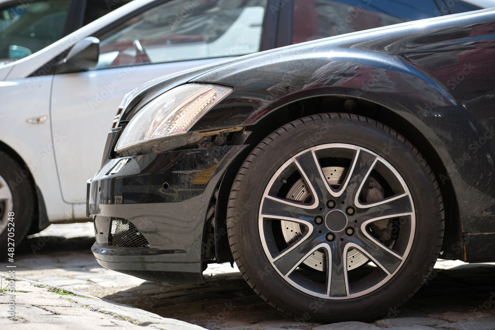 Dented car with damaged fender parked on city street side. Road safety and vehicle insurance concept