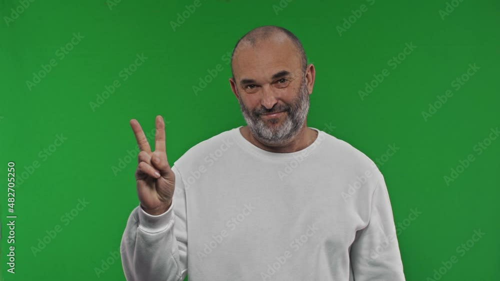 Cheerful senior man showes victory sign on isolated green background Cheerful senior man showes victory sign on isolated green background