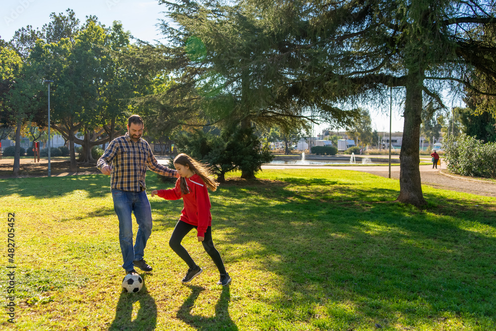 Happy father and cute smiling daughter playing soccer together at park. Happy father and cute smiling daughter playing soccer together at park.