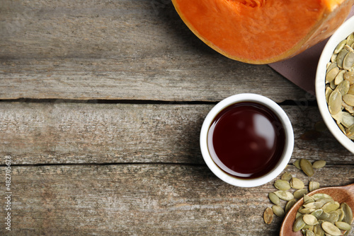 Bowl of oil and pumpkin seeds on wooden table  flat lay. Space for text