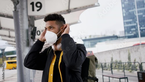 Young African- american man commuter with face mask wiating at bus station. photo