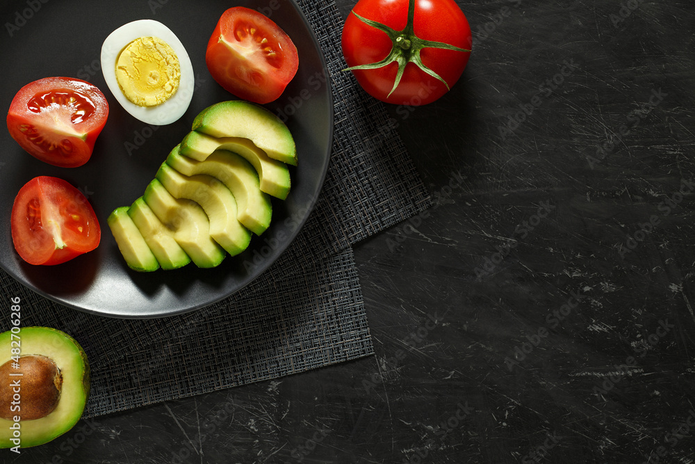 Avocado, tomatoes, egg on a gray plate, top view dark background, with space to copy text. Concept of healthy nutrition. Avocado, tomatoes, egg on a gray plate, top view dark background, with space to copy text. Concept of healthy nutrition.