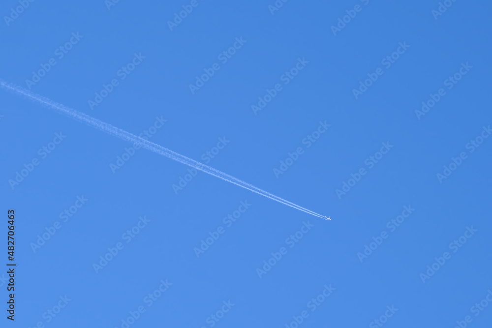 Distant passenger jet plane flying on high altitude on clear blue sky leaving white smoke trace of contrail behind. Air transportation concept Distant passenger jet plane flying on high altitude on clear blue sky leaving white smoke trace of contrail behind. Air transportation concept