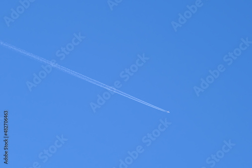 Distant passenger jet plane flying on high altitude on clear blue sky leaving white smoke trace of contrail behind. Air transportation concept