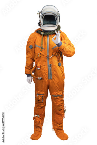 Astronaut wearing an orange spacesuit and helmet showing hand OK sign gesture isolated on white background.