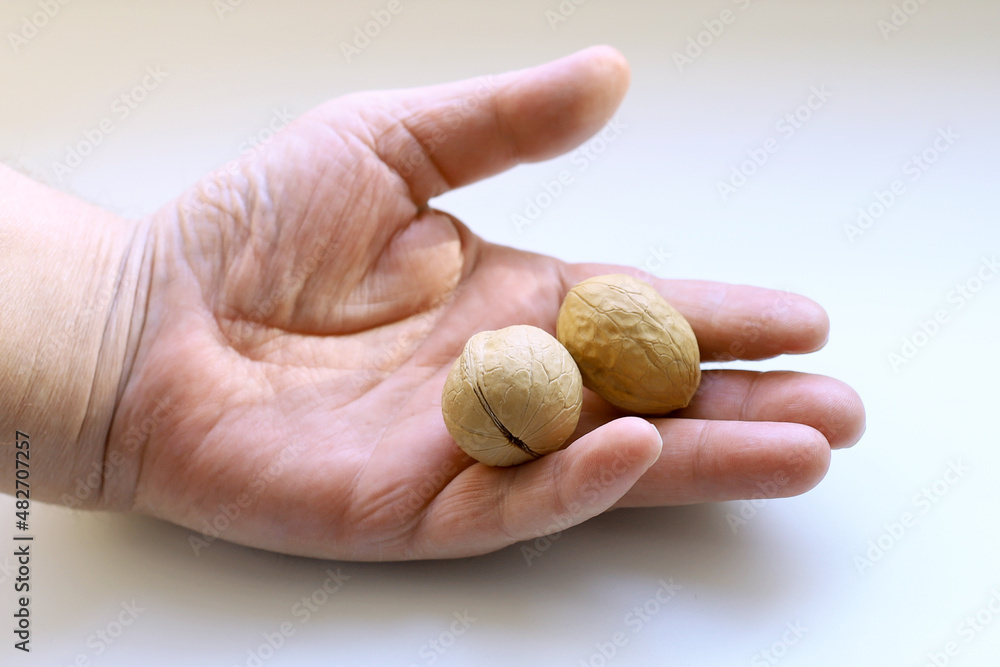 two walnuts in a man's hand, light background, close-up