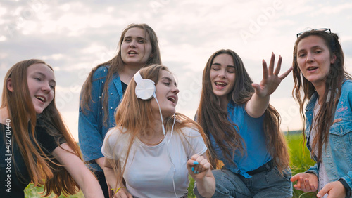 A group of girls of friends are listening to music on headphones and dancing to a friend. © Довидович Михаил