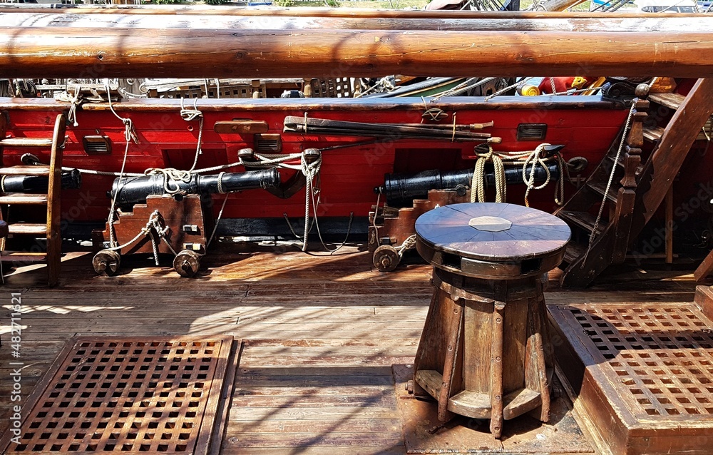 Wooden windlass and black cannons along the side of an old sailing ship