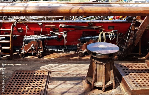 Wooden windlass and black cannons along the side of an old sailing ship