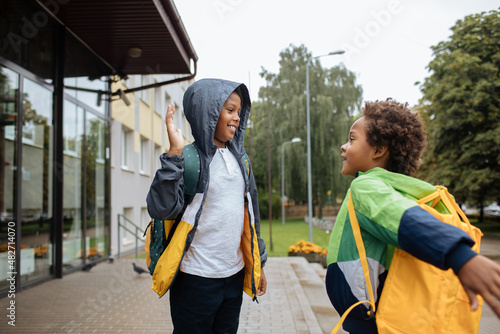 Schoolboys with backpacks. Two African American boys next to the school. Back to the school concept. Kids standing outside and happy to meet each others. Happy black children. First day of school © Girts