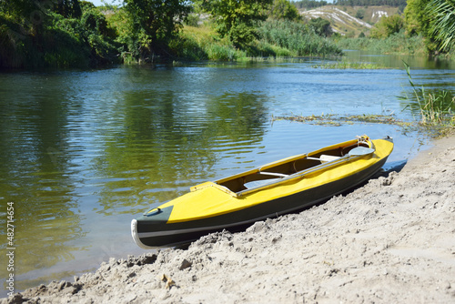 Yellow bright kayak lies on the bank of the Oskol river.