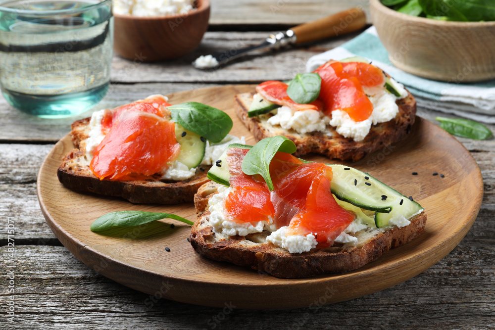 Delicious sandwiches with cream cheese, salmon, cucumber and spinach on wooden table, closeup