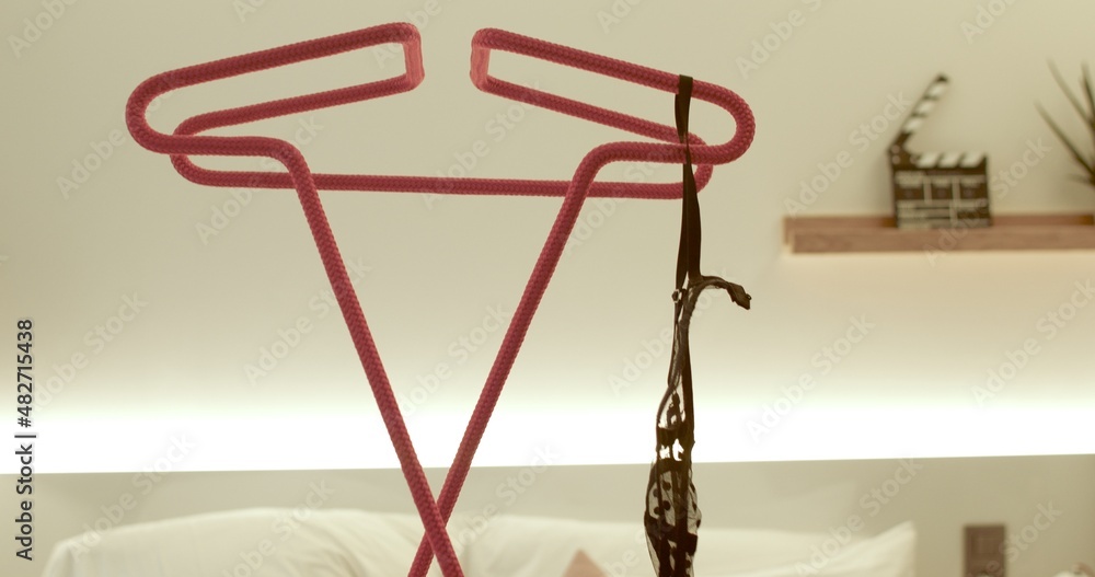A woman's hand threw her bra onto a red hanger. A place to fold clothes before bed. The garment is loose. In the background there is a bed in bokeh.
