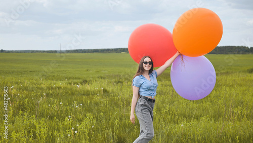 Happy girl with big multicolored balloons posing on the field.