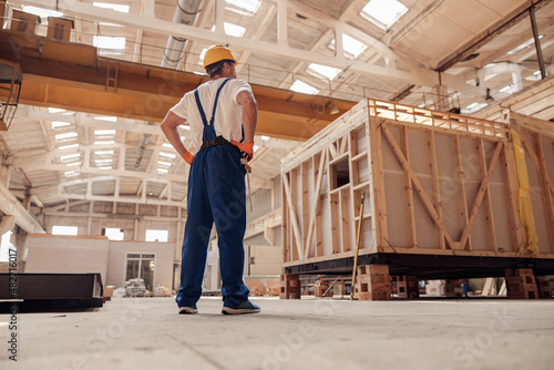 Male builder in work overalls observing building under construction