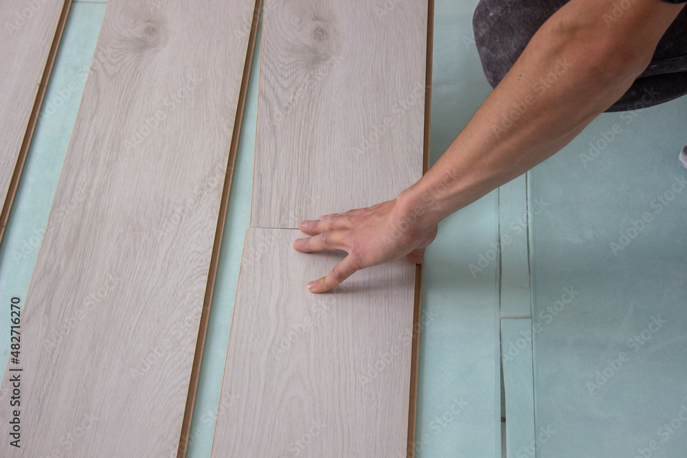 Workers' hands install a wooden laminate floor. Home renovation with wooden floors with measurements.