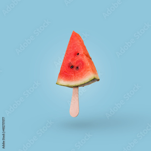 Watermelon slice on a ice cream stick isolated on bright blue background.