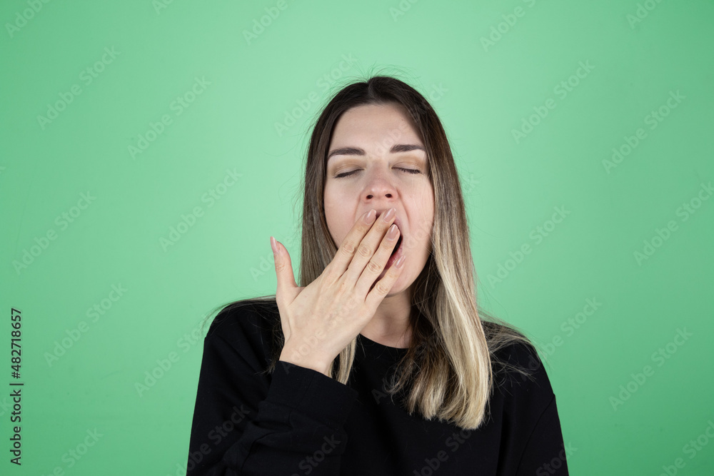 Young girl yawning. She is very overworked and sleepy. Green isolated studio background. Copy paste and text space. Young girl yawning. She is very overworked and sleepy. Green isolated studio background. Copy paste and text space.