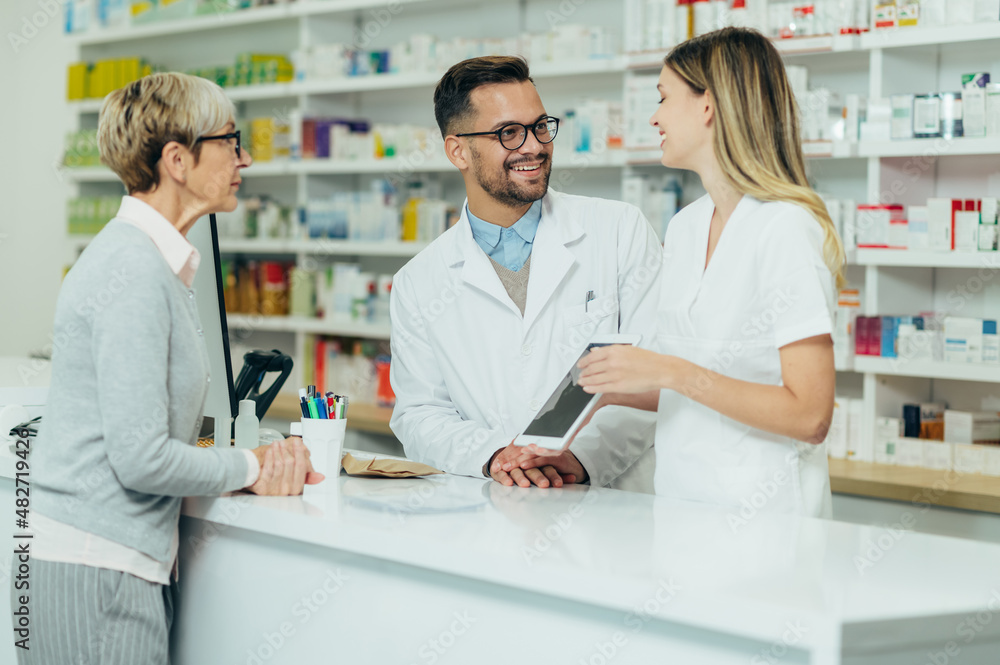 Two pharmacist giving prescription medications to senior female customer in a pharmacy