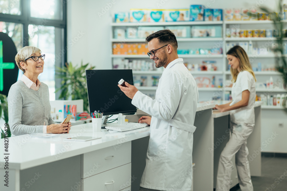 Young male pharmacist giving prescription medications to senior female customer in a pharmacy