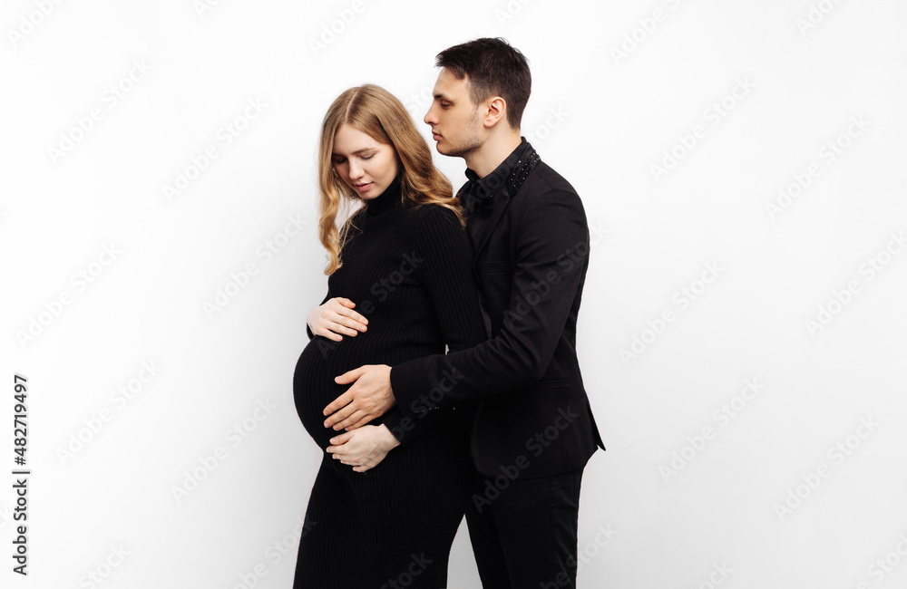 man stands behind his pregnant wife and smiles, hugging her on a white isolated background man stands behind his pregnant wife and smiles, hugging her on a white isolated background