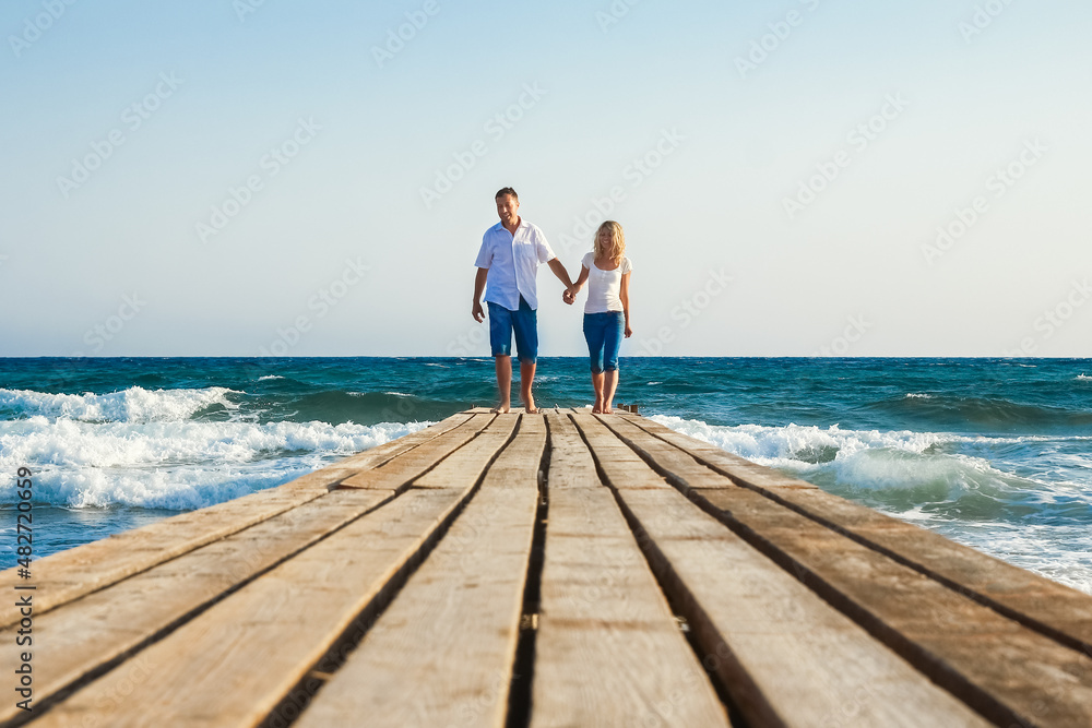 A The guy and the girl are walking along the pier at the sea in nature journey