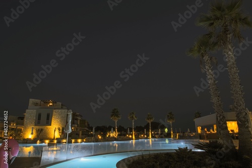 Beautiful night landscape view of hotel area. Lighting, trees, swimming pool modern buildings on dark sky background. Greece. 