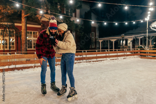 Multiracial couple using phone while ice skating