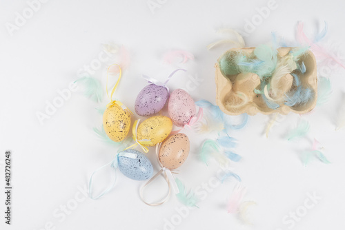 chicken, painted eggs for Easter, lie in a box and next to each other, decorated with colored feathers on a white background.There is space for text