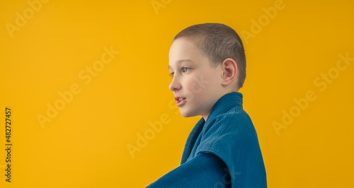 boy in blue sportswear stands sideways and looks to the side, yellow background photo