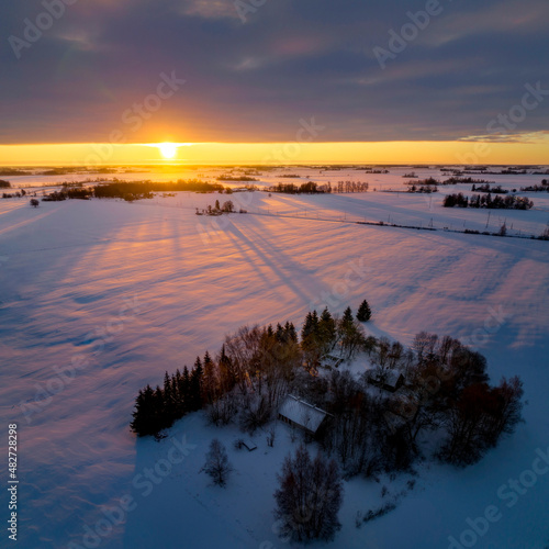 Aerial photos of sunrise over forest and fields during winter