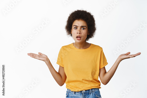 Confused young african american girl shrugging shoulders, looking clueless and annoyed, cant understand why, what happened, white background