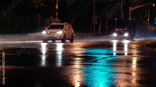 Rainy night in city, cars driving on wet road, rain was illuminated by the headlights of cars, focused on the asphalt road.