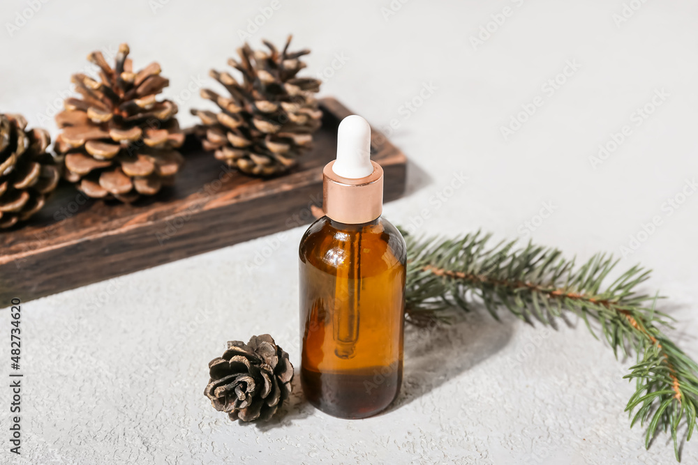 Bottle with essential oil, fir branch and pine cones on light background Bottle with essential oil, fir branch and pine cones on light background