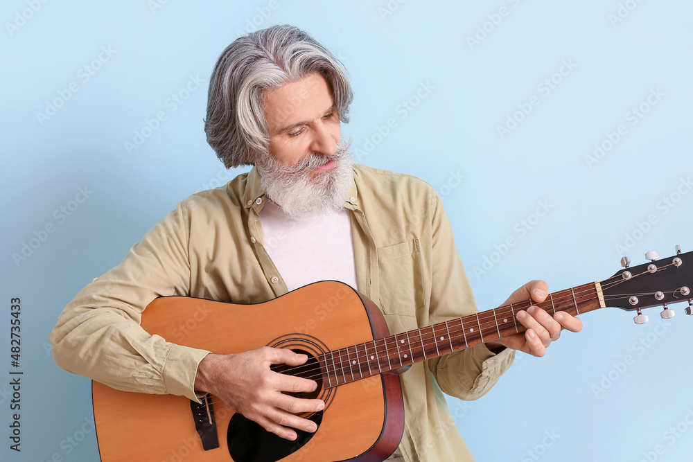 Fototapeta premium Bearded senior man playing guitar on blue background