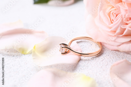 Beautiful golden engagement ring with rose petals on light background, closeup