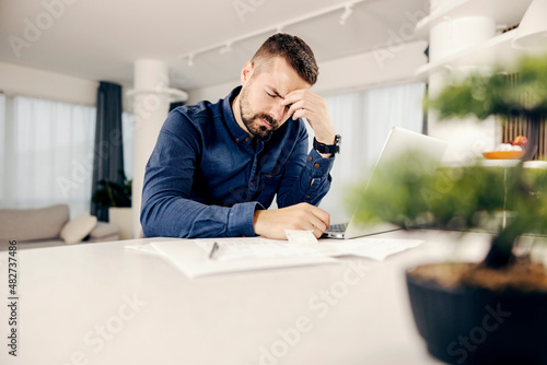 A man having headache and migraine while doing paperwork and bills from home.