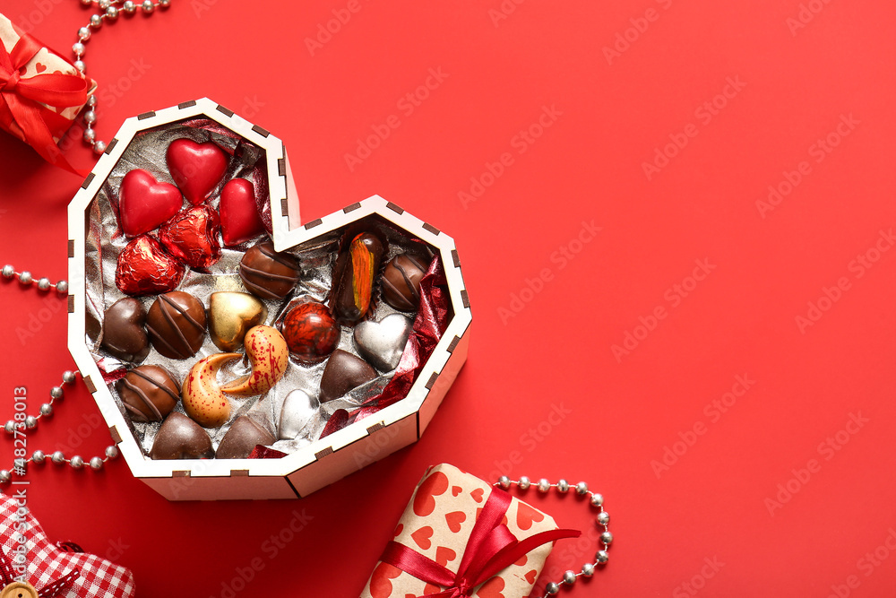Naklejka premium Heart shaped box with tasty chocolate candies on red background