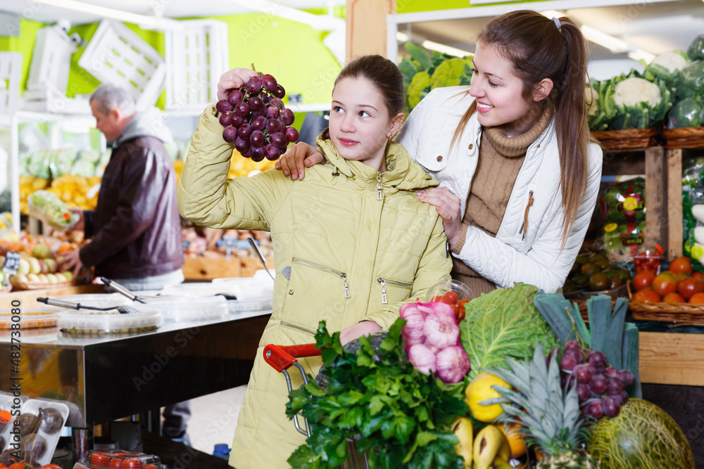 Smiling girl and young mother looking for fresh delicious fruits during family shopping