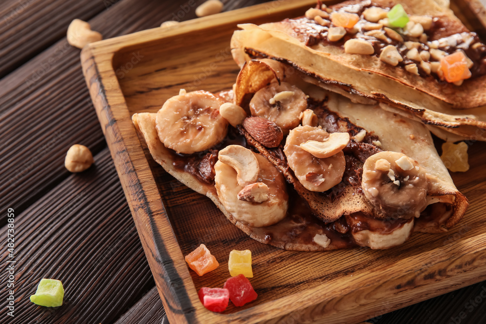 Board of tasty thin pancakes with chocolate paste and nuts on dark wooden background, closeup
