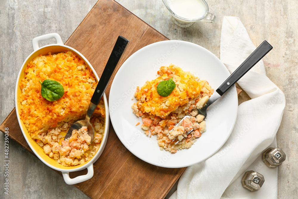 Plate and baking dish with tasty English fish pie on grey background Plate and baking dish with tasty English fish pie on grey background