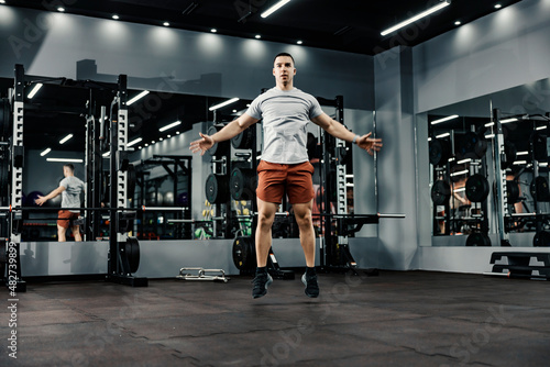 A strong sportsman doing jumping jacks in a gym. Fitness and gym workout.