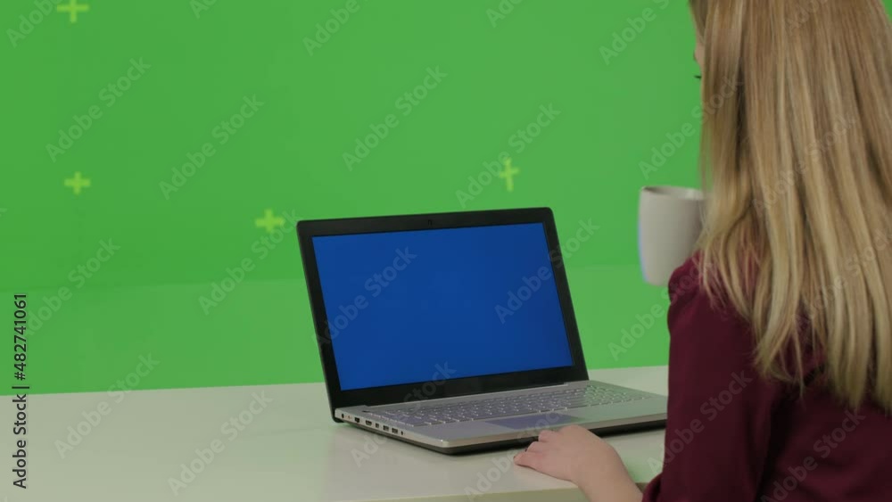 Business woman sits in a home chair and uses a computer with blue screen over green wall . Remote work. Social distance. Girl studying,l blogging, communicating with clients or doctor or psychiatrist Business woman sits in a home chair and uses a computer with blue screen over green wall . Remote work. Social distance. Girl studying,l blogging, communicating with clients or doctor or psychiatrist