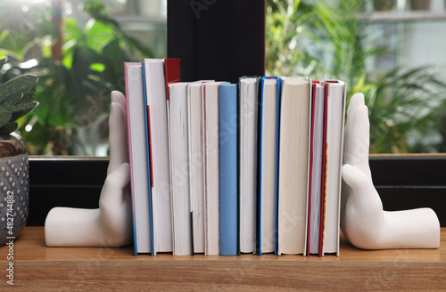 Beautiful hand shaped bookends with books on window sill indoors photo