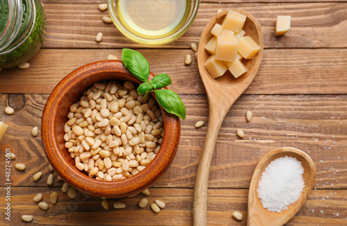 Bowl of tasty pine nuts and ingredients for pesto sauce on wooden background