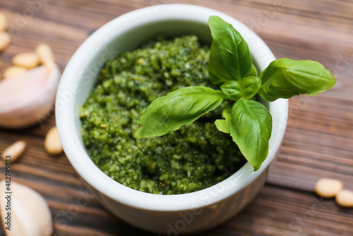 Bowl of tasty pesto sauce and ingredients on wooden background